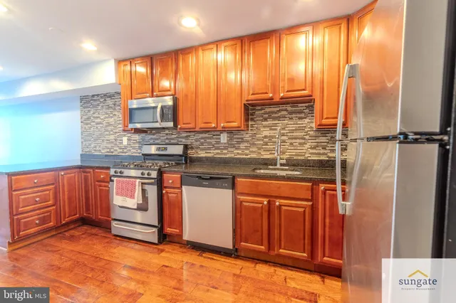a kitchen with stainless steel appliances granite countertop a refrigerator a sink and wooden cabinets