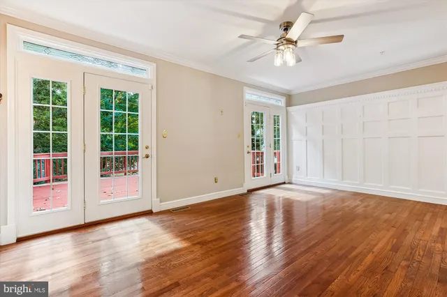 a view of an empty room with wooden floor ceiling fan