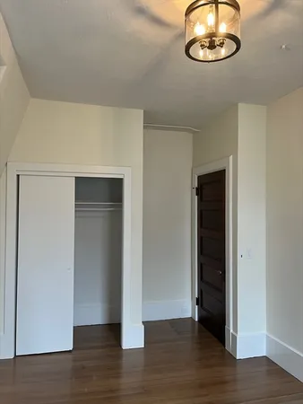 an empty room with wooden floor and way to kitchen