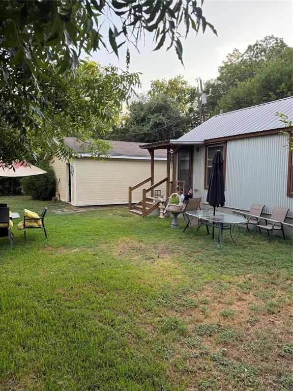 300 Northwest 3rd Street Hubbard, TX 76648 - Photo 21 of 25 Expansive green space featuring a detached building with an overhead door, a covered porch, and a main structure with a metal roof