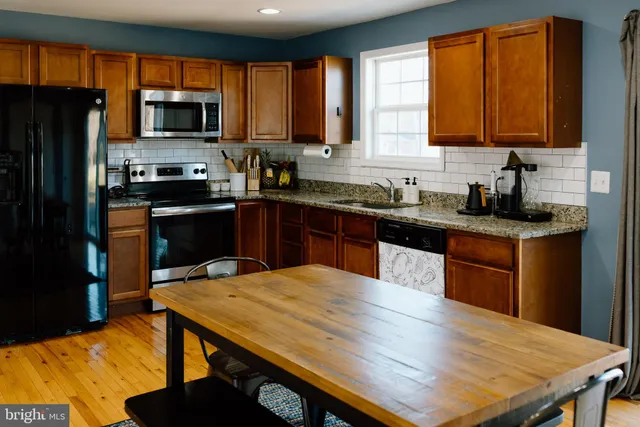 a kitchen with stainless steel appliances kitchen island granite countertop a sink dishwasher a stove top oven a refrigerator with grey cabinets and wooden floor