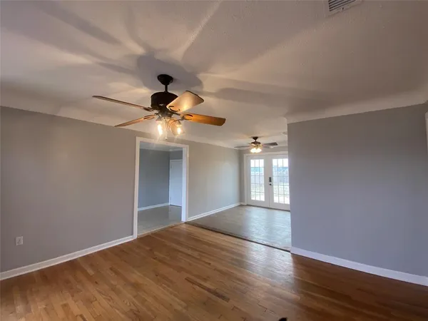 a view of an empty room with wooden floor and a ceiling fan