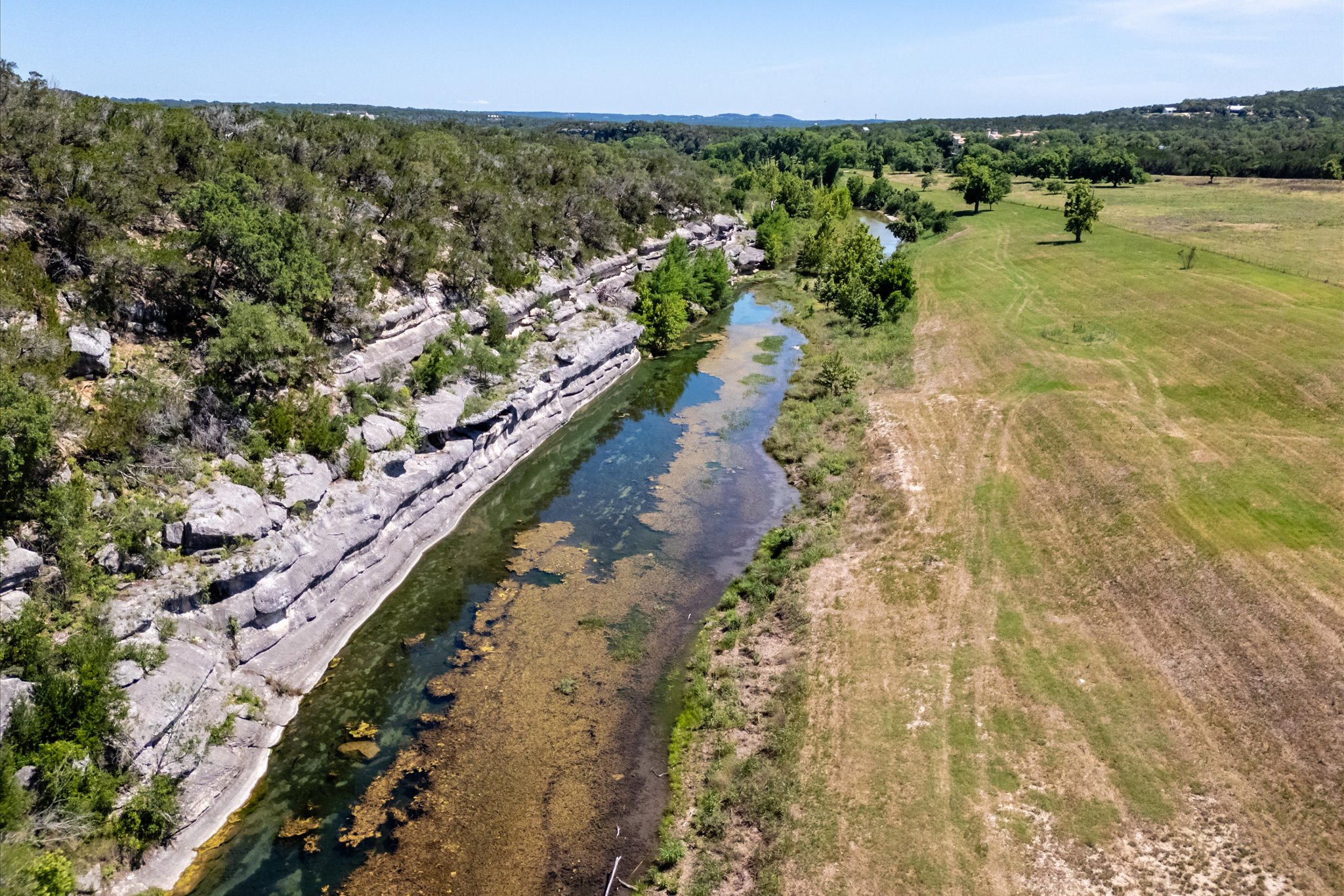 4698 Fischer Store Road Wimberley, TX 78676 - Photo 28 of 28 Dramatic rocky cliffs border a serene flowing river winding through rolling green countryside.