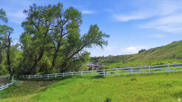 2075 Canyon Road Smithfield, UT 84335 - Photo 18 of 18 Expansive green landscape featuring a white fence, mature deciduous trees, and a sloping hillside