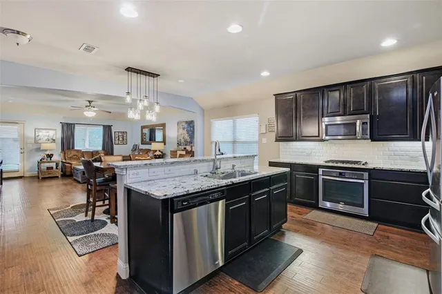 a kitchen with stainless steel appliances granite countertop a stove top oven a sink dishwasher a dining table and chairs with wooden floor