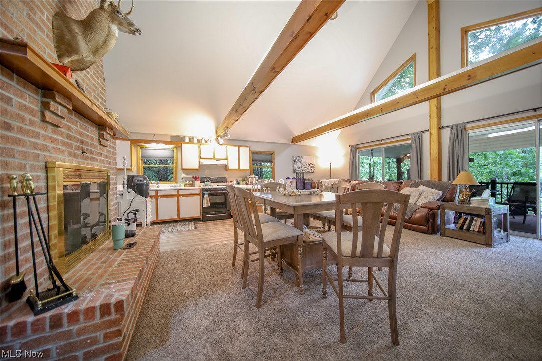Dining area with brick wall, a fireplace, light carpet, vaulted ceiling with beams, and a high ceiling