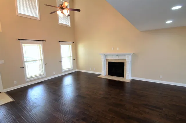 an empty room with wooden floor a chandelier fan and windows