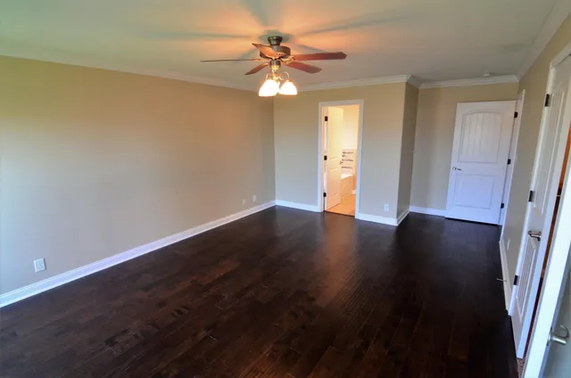 a view of an empty room with wooden floor and a ceiling fan