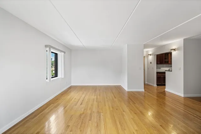 a view of empty room with wooden floor and kitchen