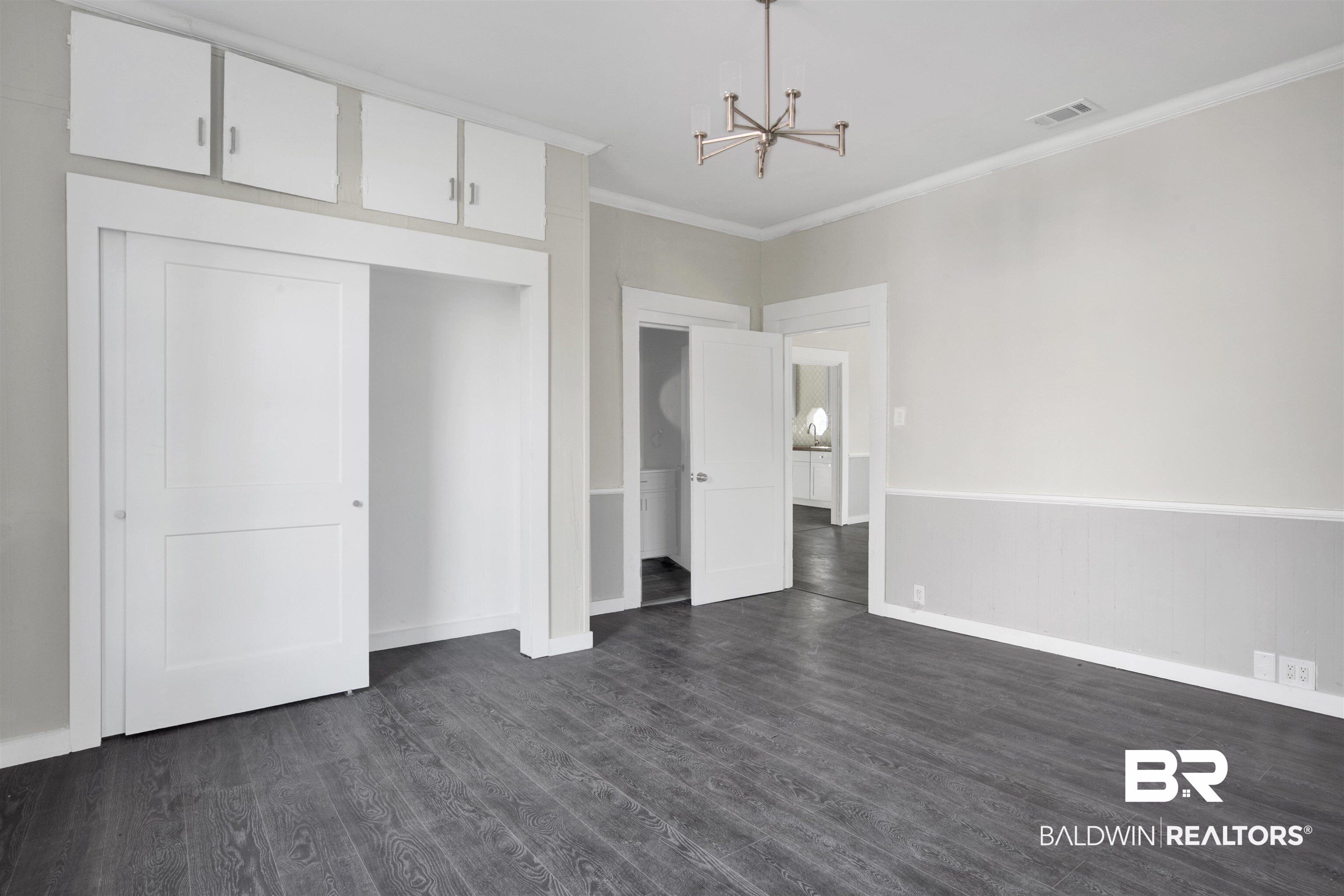 1063 Selma Street Mobile, AL 36604 - Photo 15 of 32 Unfurnished bedroom with crown molding, a chandelier, dark wood-style flooring, a closet, and wainscoting