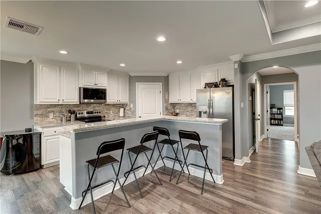 a kitchen with stainless steel appliances granite countertop a refrigerator a sink dishwasher a stove and white cabinets with wooden floor