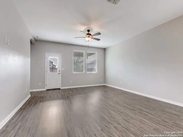 an empty room with wooden floor ceiling fan and windows