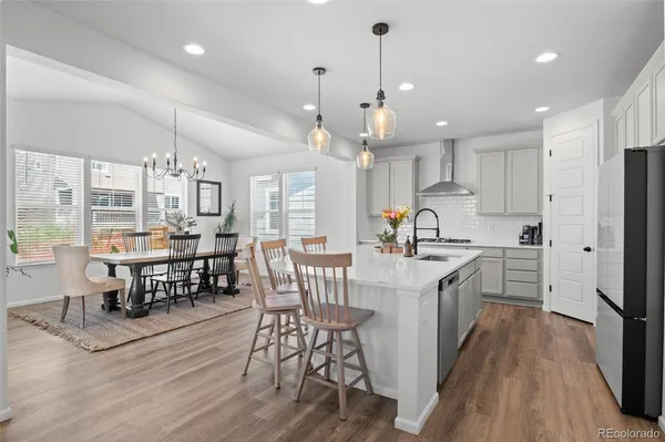 a kitchen with stainless steel appliances granite countertop a stove a refrigerator a kitchen island a dining table and chairs with wooden floor