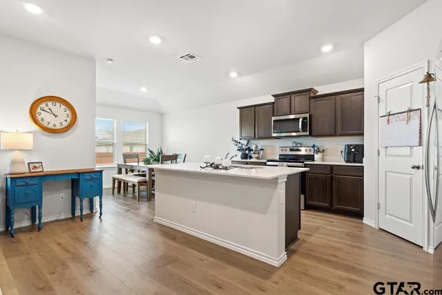 a open kitchen with stainless steel appliances granite countertop a stove top oven a sink a dining table and chairs with wooden floor