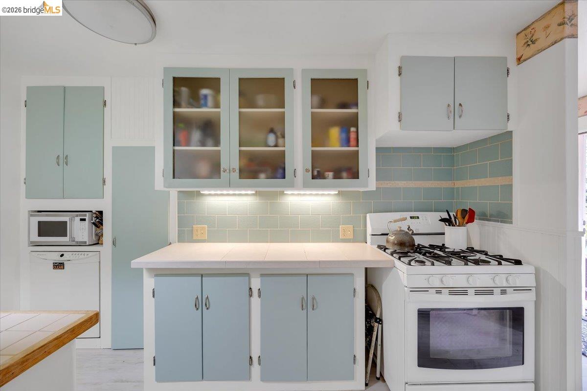26144 Long Barn Road Long Barn, CA 95335 - Photo 14 of 42 Light blue cabinetry with glass-front upper cabinets, tile backsplash, under-cabinet lighting, and a built-in gas range