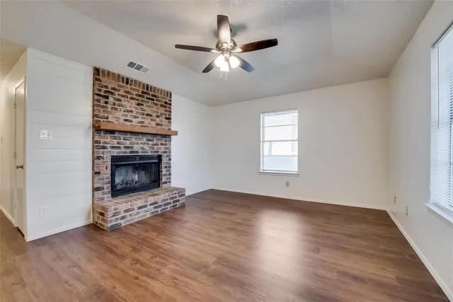 a view of an empty room with wooden floor a fireplace and a window