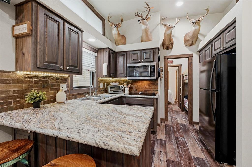 3958 Ranch Road Whitesboro, TX 76273 - Photo 12 of 40 Kitchen featuring dark wood-finish cabinetry, light-toned stone-finish countertops, and a brick-patterned backsplash