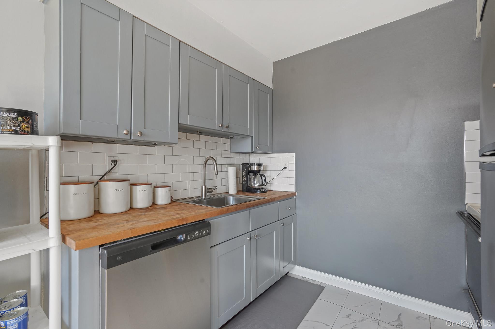 26 Cooper Road, Unit 411 Poughkeepsie, NY 12603 - Photo 9 of 17 Kitchen featuring gray cabinets, dishwasher, wood counters, backsplash, and light marble finish flooring