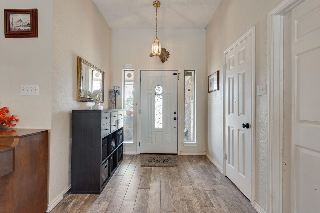 83 Crown Road Willow Park, TX 76087 - Photo 3 of 35 Vaulted entry with wood-finish flooring, white paneled entry door, two sidelight windows, and a hanging brass-finish light fixture