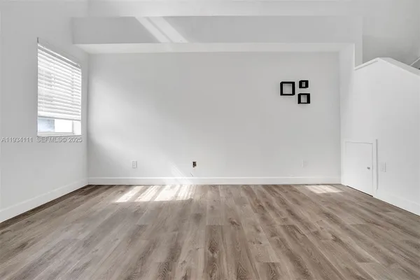 a view of an empty room with wooden floor and a window