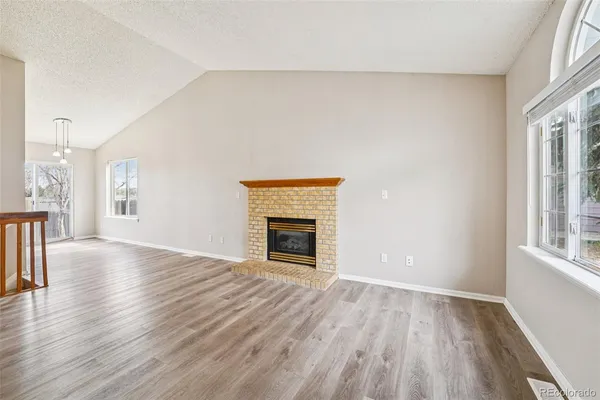 an empty room with wooden floor fireplace and windows