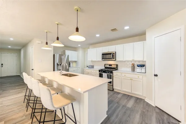 a kitchen with stainless steel appliances kitchen island granite countertop a sink a stove a refrigerator and white cabinets with wooden floor