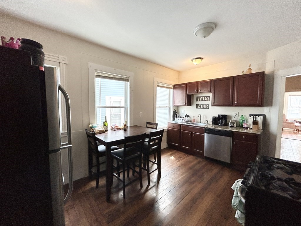 a kitchen with stainless steel appliances granite countertop a refrigerator a sink dishwasher a stove a dining table and chairs with wooden floor