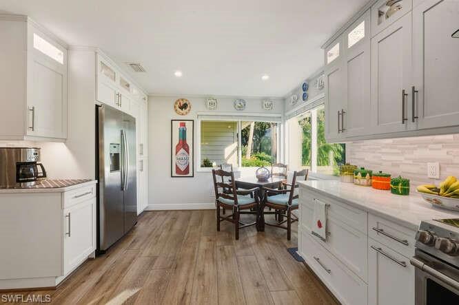 254 Edgemere Way East Naples, FL 34105 - Photo 15 of 41 Kitchen featuring glass insert cabinets, decorative backsplash, appliances with stainless steel finishes, light wood-style flooring, and white cabinetry