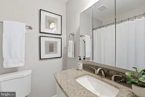 a bathroom with a granite countertop sink a mirror a shower and a toilet