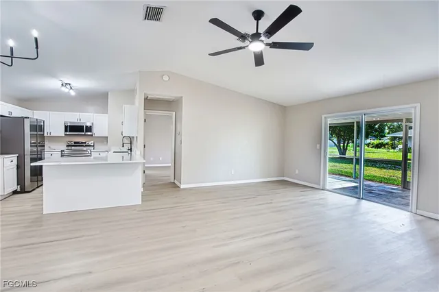 a view of an empty room with kitchen and window