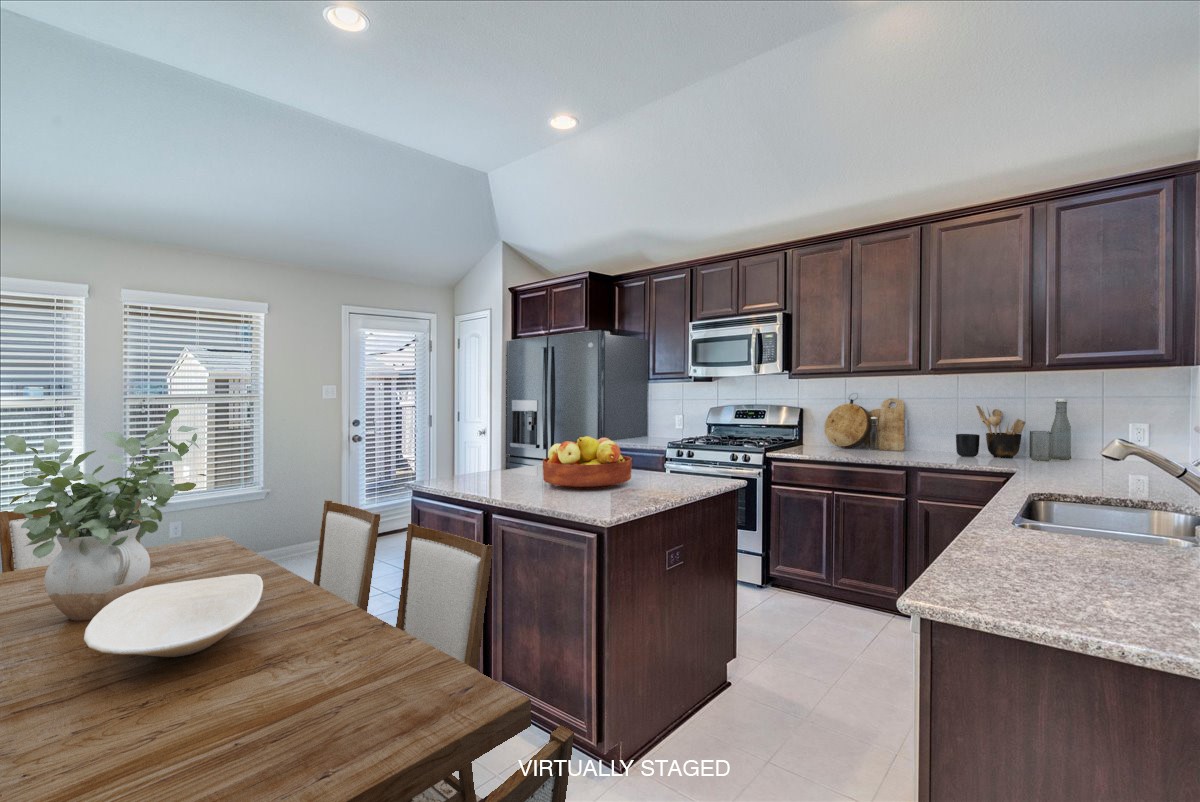 161 Mistflower Lane Kyle, TX 78640 - Photo 10 of 37 Kitchen featuring dark wood finish cabinetry, stainless steel appliances, a center island, lofted ceiling, and light stone countertops