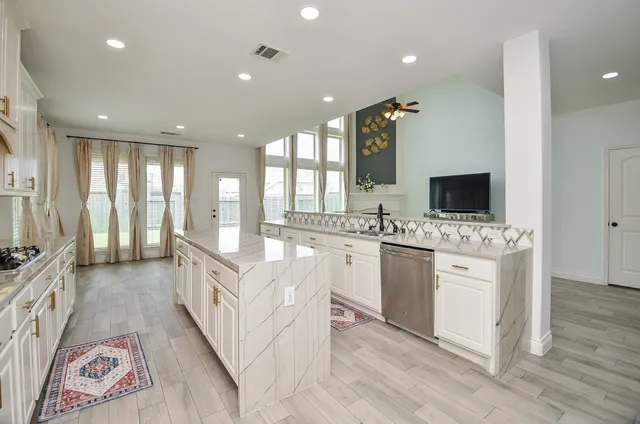 a kitchen with stainless steel appliances kitchen island granite countertop a stove a sink a refrigerator and white cabinets with wooden floor