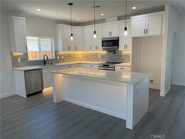 a kitchen with stainless steel appliances granite countertop a stove a sink a refrigerator and white cabinets with wooden floor