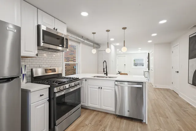 a kitchen with stainless steel appliances a stove top oven a sink dishwasher a refrigerator white cabinets and wooden floor