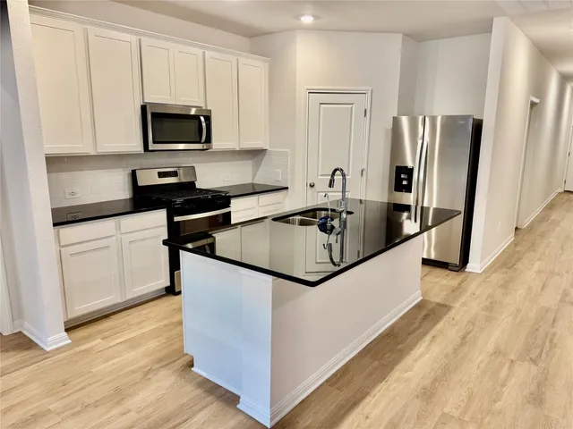 a kitchen with granite countertop a refrigerator a sink a stove a microwave and wooden floor