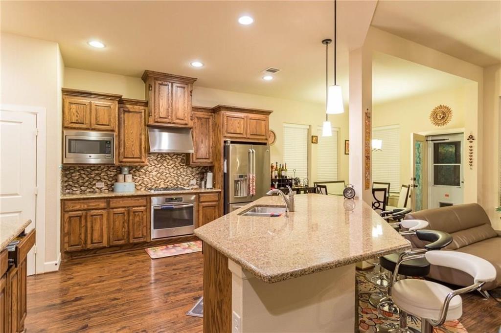 423 Palacio Street Irving, TX 75039 - Photo 18 of 18 Kitchen featuring tasteful backsplash, a kitchen breakfast bar, brown cabinetry, dark wood-type flooring, and appliances with stainless steel finishes