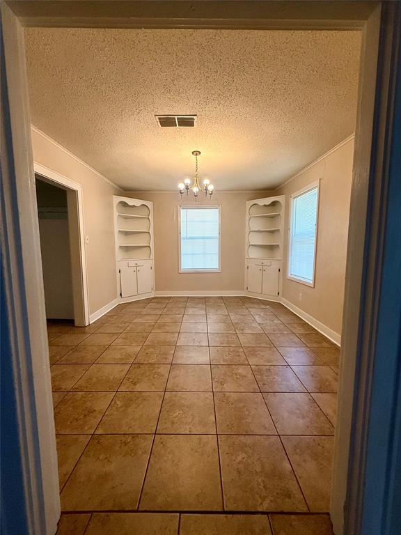 217 3rd St Pinehill Springhill, LA 71075 - Photo 4 of 23 Spacious room featuring tile flooring, a brass chandelier, and two built-in shelving units flanking windows