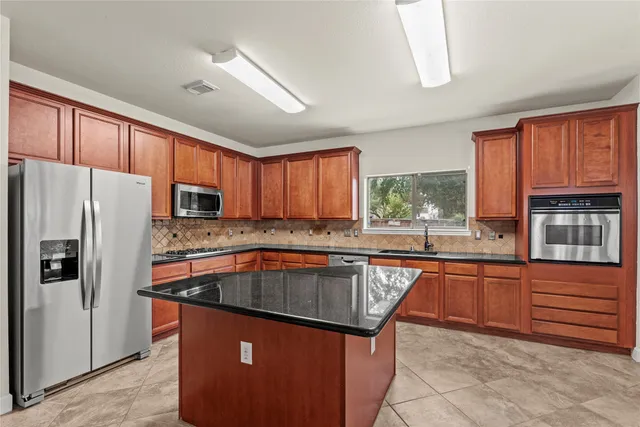 a kitchen with stainless steel appliances granite countertop a refrigerator a sink dishwasher a stove and a refrigerator