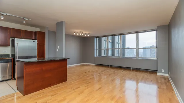 a view of an empty room with kitchen and a window