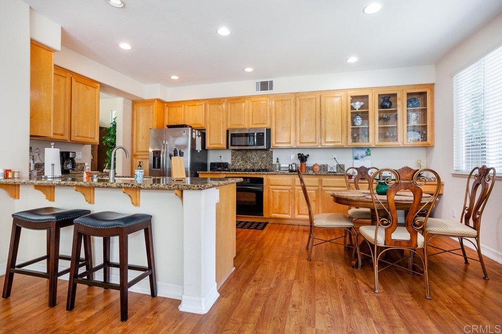 5560 Foxtail Loop Carlsbad, CA 92010 - Photo 4 of 32 a kitchen with stainless steel appliances granite countertop table chairs stove and wooden floor
