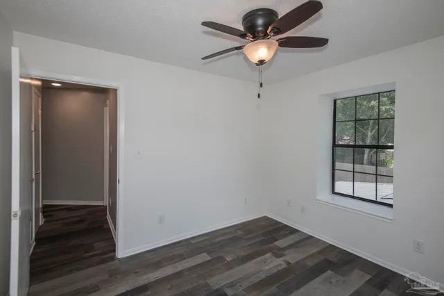 an empty room with wooden floor chandelier fan and windows