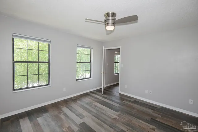 an empty room with wooden floor windows and fan