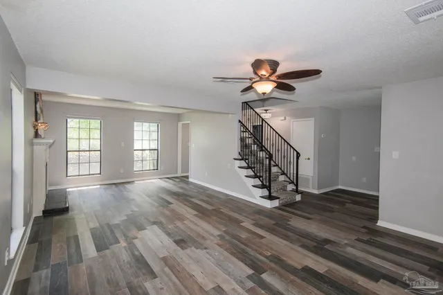 a view of an empty room with chandelier fan and wooden floor