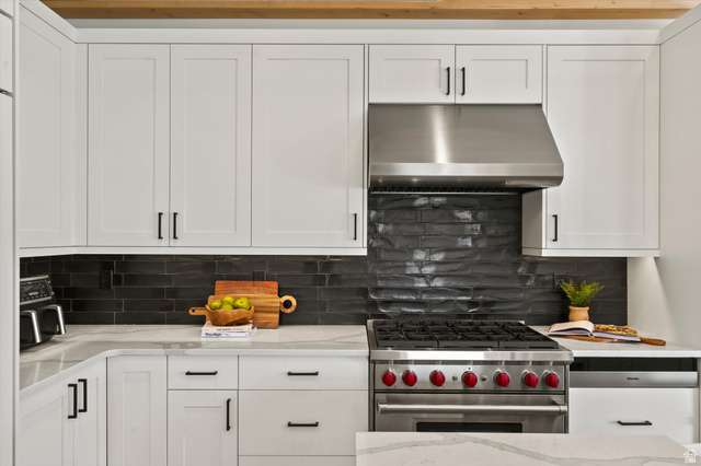 4499 North Seven Bridges Road, Unit 9 Eden, UT 84310 - Photo 10 of 65 White shaker-style cabinetry, stainless steel range hood, dark textured backsplash, professional-grade gas range, and light-toned countertops