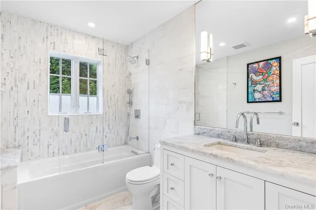 a bathroom with a granite countertop sink a toilet a mirror a bathtub and shower