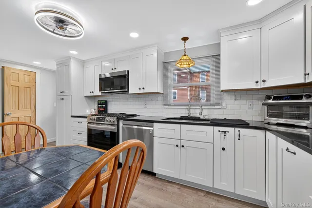 a kitchen with stainless steel appliances granite countertop a stove top oven a sink a dining table and chairs with white cabinets