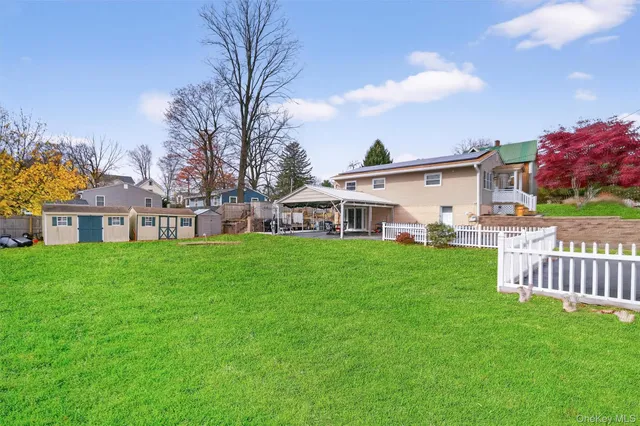 a view of a white house in front of a big yard with plants and large trees