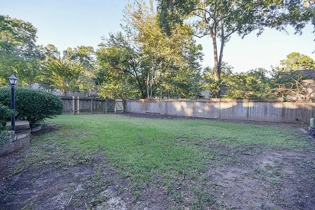 a view of a backyard with large trees and wooden fence