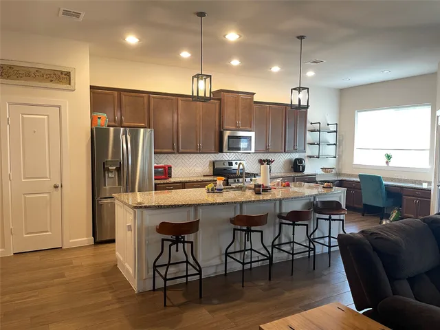 a kitchen with stainless steel appliances kitchen island granite countertop a refrigerator a stove a sink a dining table and chairs with wooden floor