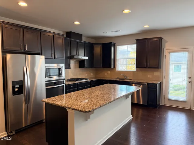 a kitchen with kitchen island granite countertop stainless steel appliances and wooden cabinets